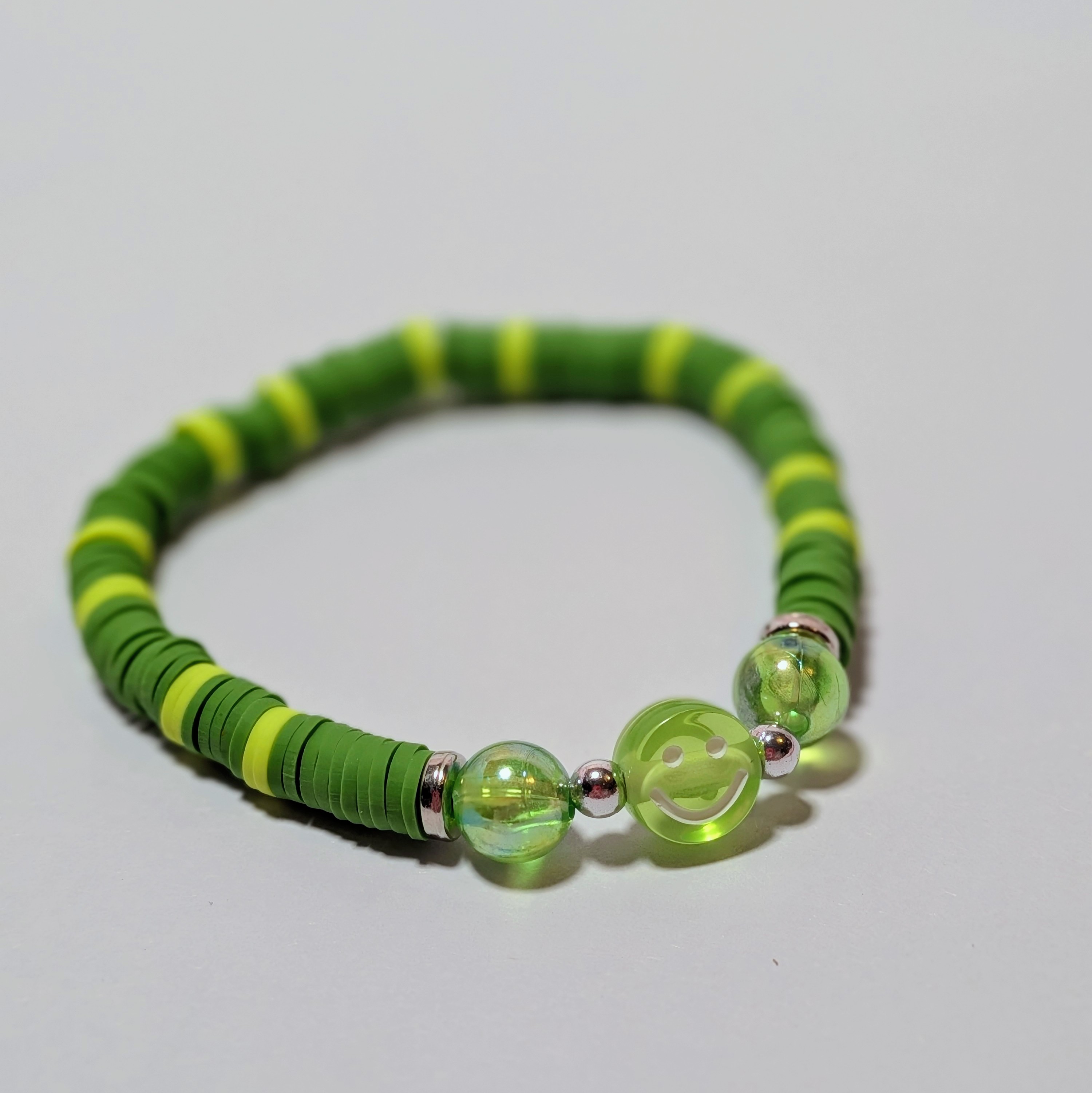 a green smiley bead surrounded by matching and contrasting clay beads