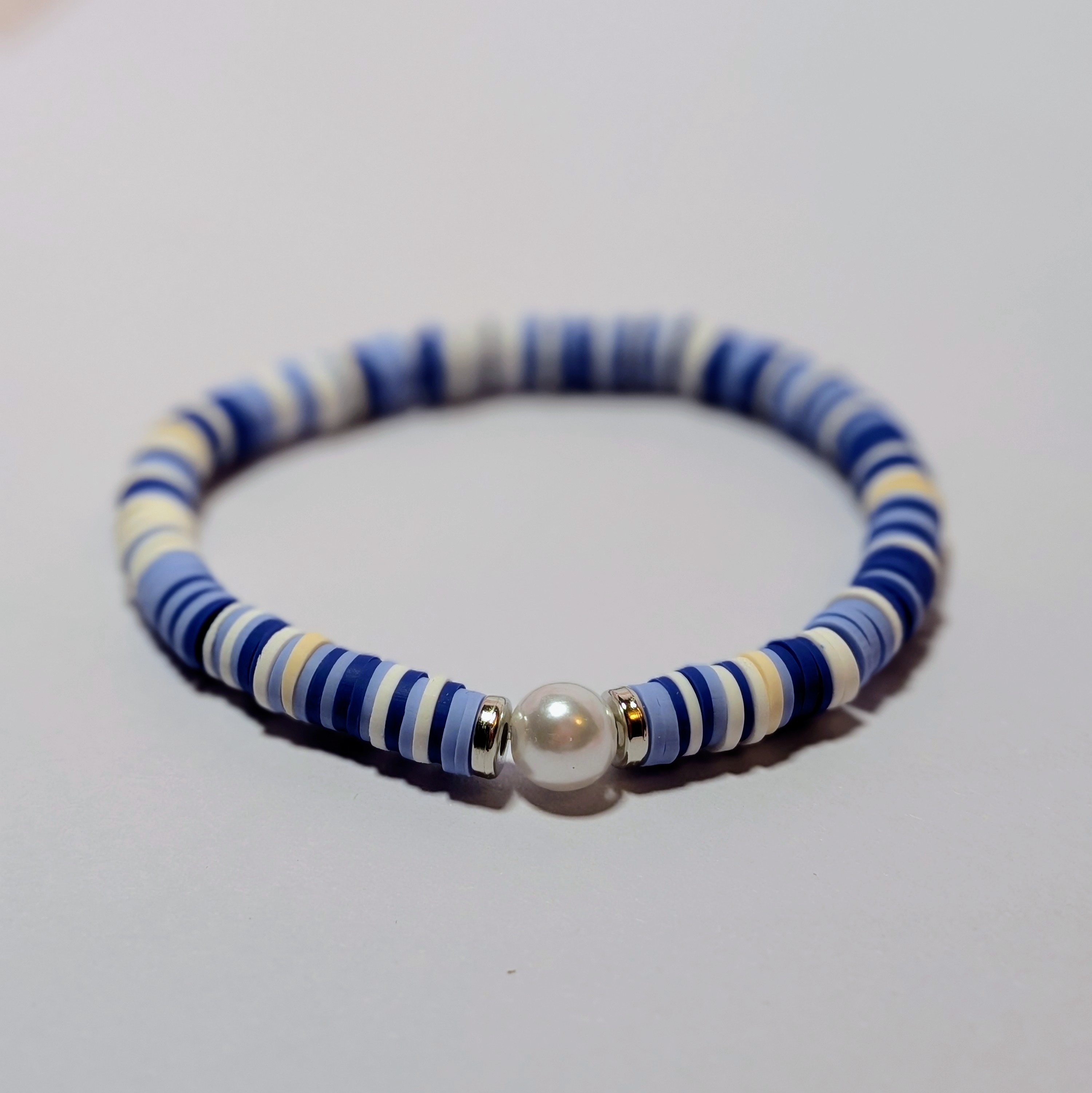 blue clay beads and silver accents surrounding a white pearl like bead