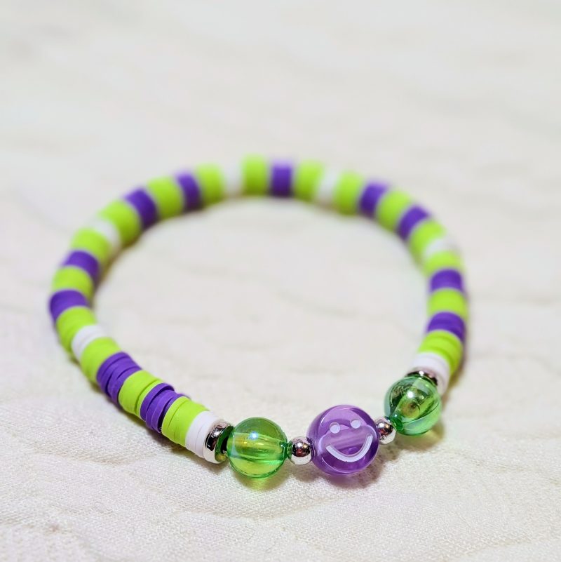 Clay friendship bracelet with purple, green and white clay beads with silver accents, round green beads and a purple smiley bead