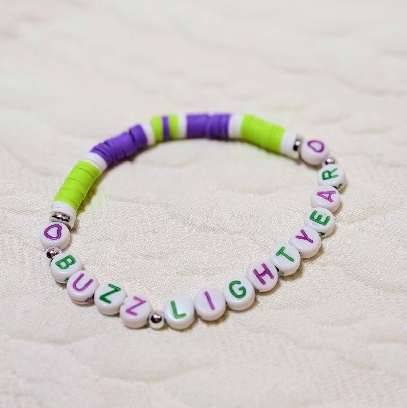Clay friendship bracelet with purple, green and white beads, with silver accents and matching purple and green letter beads saying "buzz lightyear"