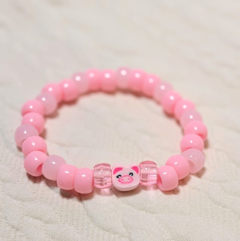 A pink pig bead surrounded by thick beads in pink, light pink and clear pink