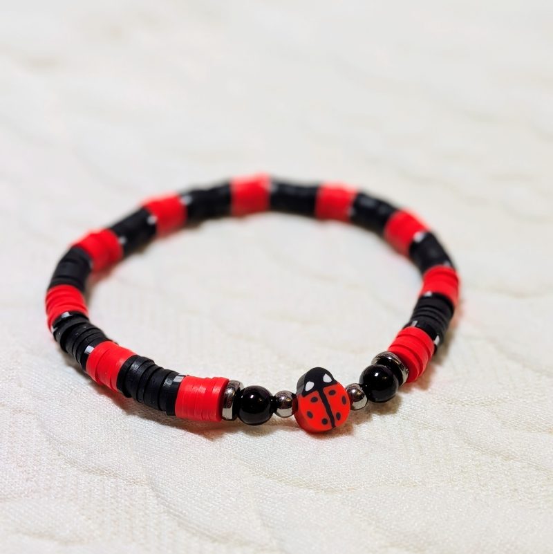 A ladybird bead surrounded by black and red clay beads, and black metallic accents.