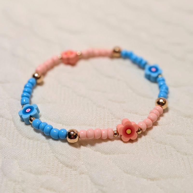 A dainty frienship bracelet with light blue and pink beads, gold accents, and four clay flower beads matching the beads.