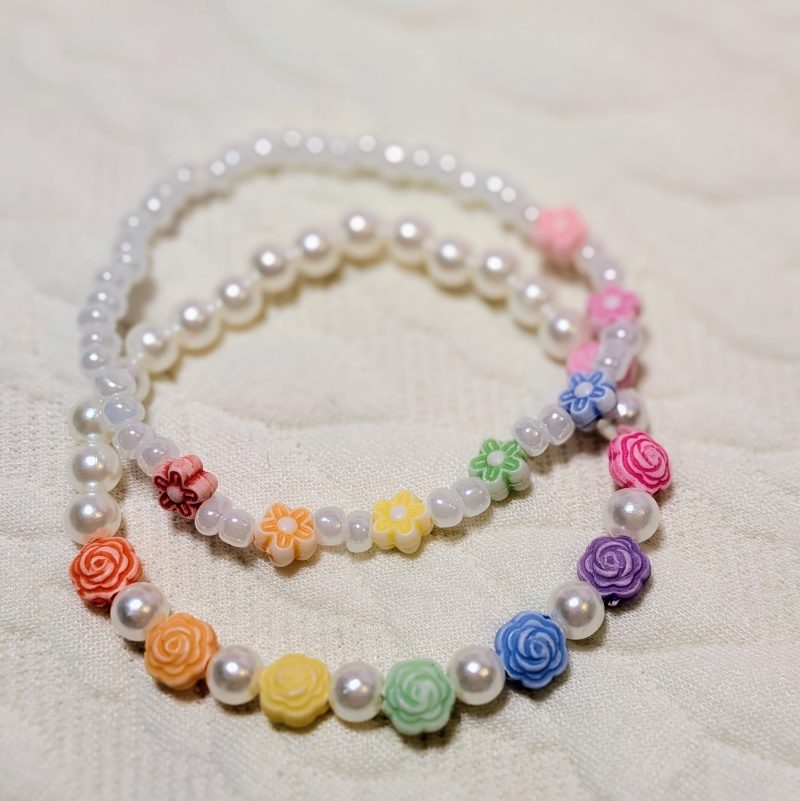 A duo of bracelets. One with larger beads and one with smaller dainty beads. Both with a rainbow of colours set between pearly white and dainty white beads.