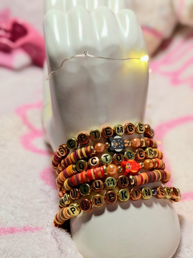 A bracelet that says "Autumn" in gold and bronze letters, with clay beads, and gold spacers — view 4