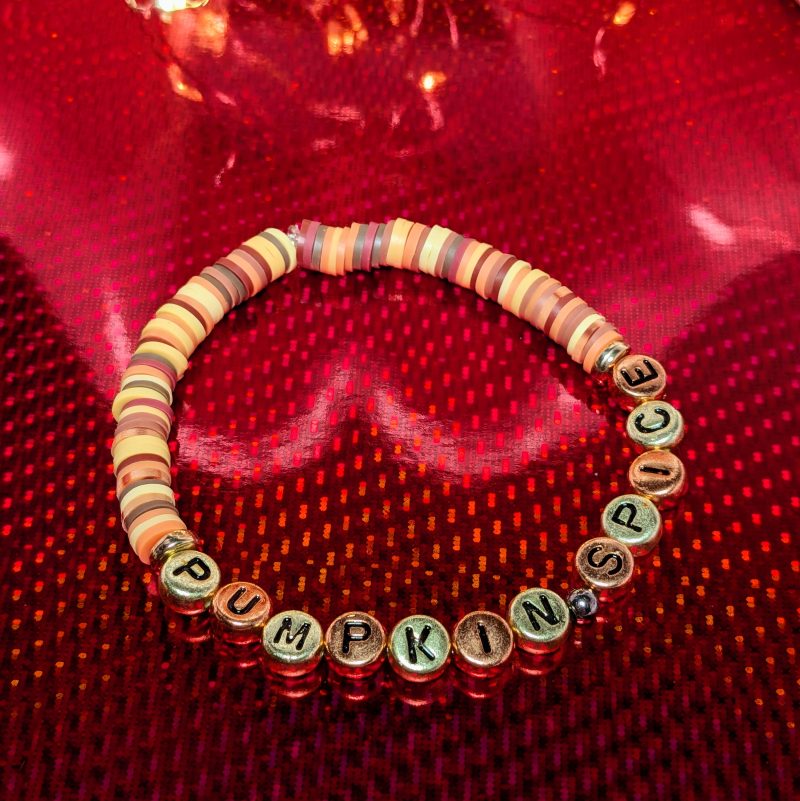 A bracelet that says "Pumpkin spice" in gold and bronze letters, with clay beads and gold spacers — view 2