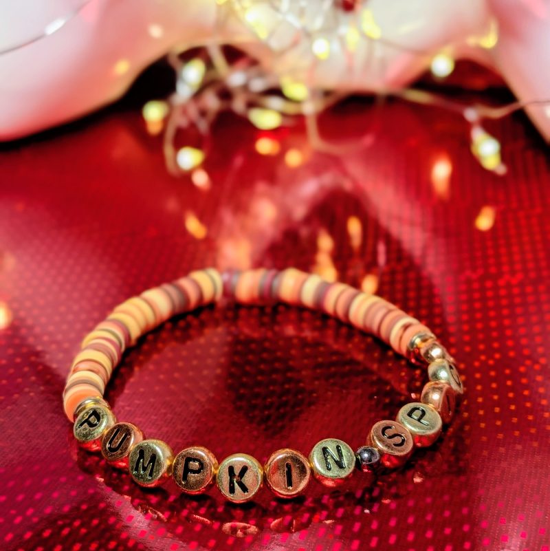 A bracelet that says "Pumpkin spice" in gold and bronze letters, with clay beads and gold spacers