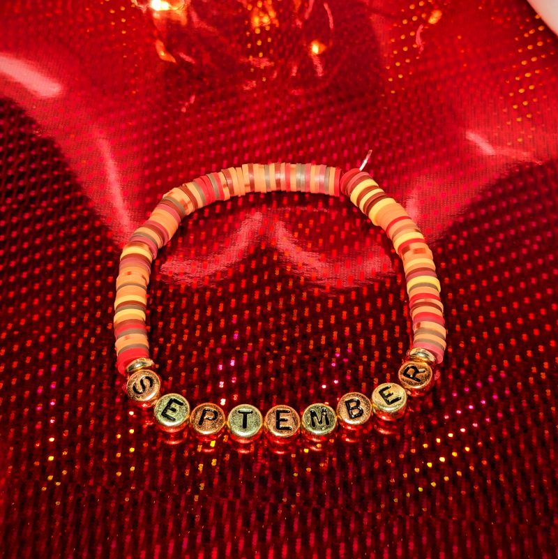 A bracelet that says "September" in gold and bronze letters with clay beads and gold spacers — view 2
