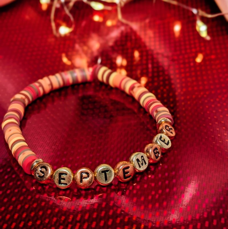 A bracelet that says "September" in gold and bronze letters with clay beads and gold spacers