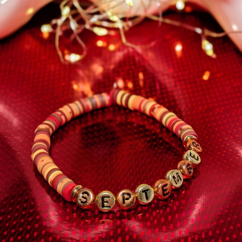 A bracelet that says "September" in gold and bronze letters with clay beads and gold spacers — view 3