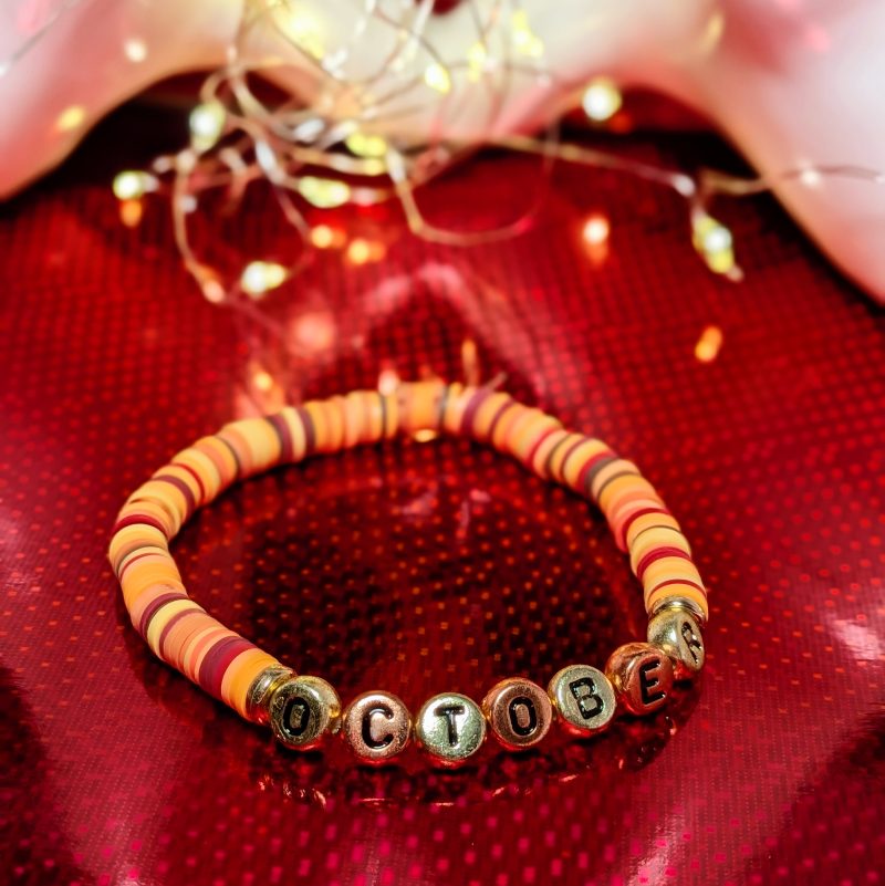 A bracelet that says "October" in gold and bronze letters, with clay beads, and gold spacers — view 3