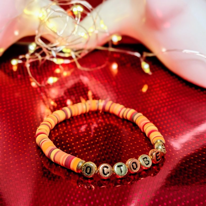 A bracelet that says "October" in gold and bronze letters, with clay beads, and gold spacers