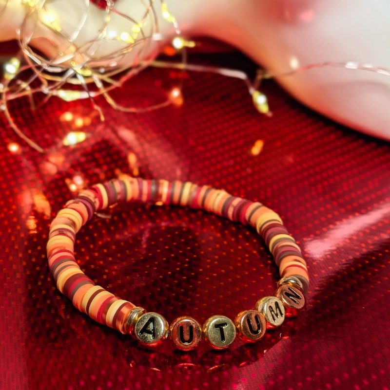 A bracelet that says "Autumn" in gold and bronze letters, with clay beads, and gold spacers — view 3