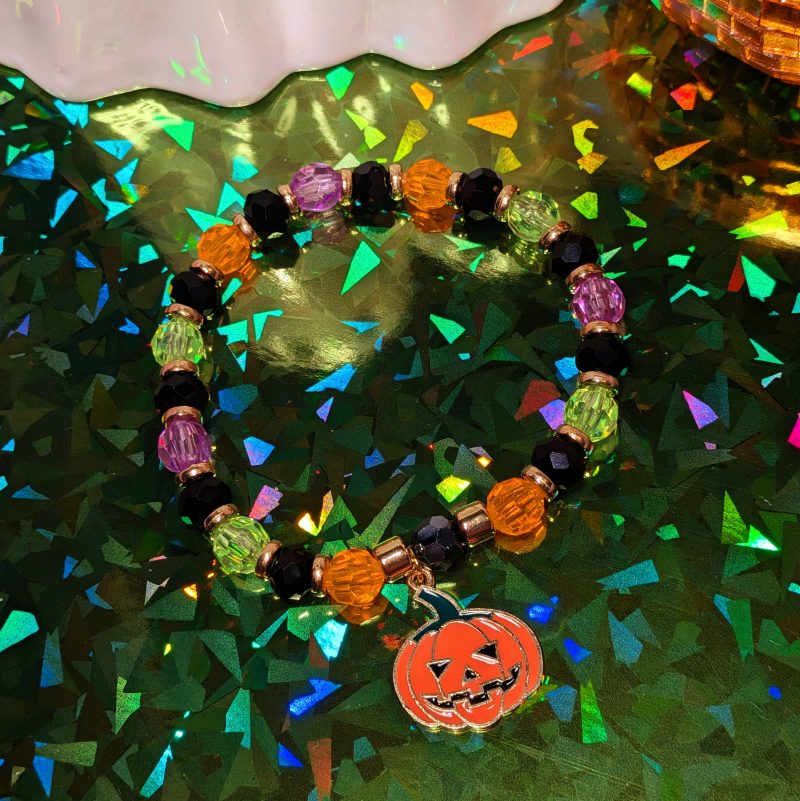 Halloween friendship bracelet with a pumpkin charm. Gold accent spacers and beads in black, orange, green, and purple. — view 4