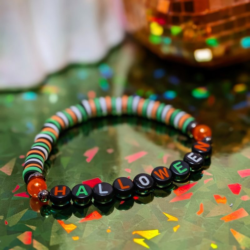friendship bracelet that spells Halloween with green, white, black and orange beads — view 2